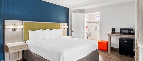 A hotel room with a large bed, bedside tables, a small kitchenette, and a bathroom visible through an open door.