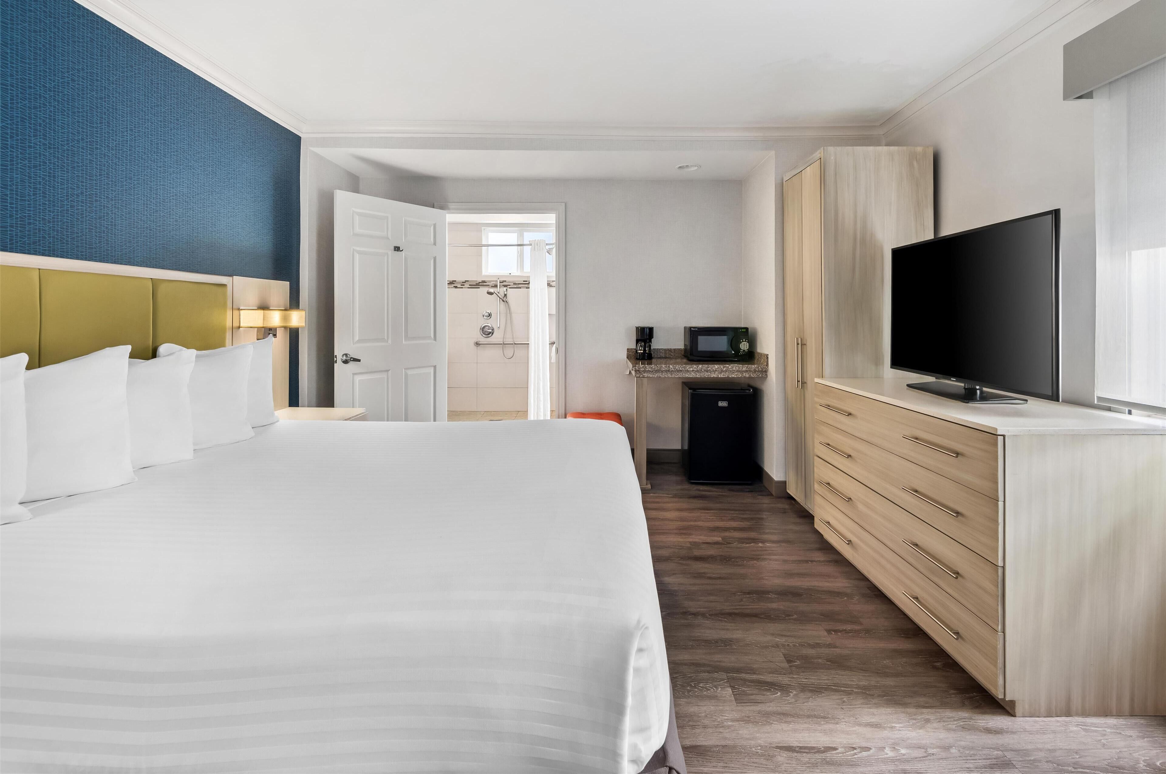 Ein Hotelzimmer mit einem großen Bett, einem Fernseher, einer Minibar und einem durch eine offene Tür einsehbaren Badezimmer.