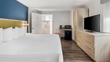 Habitación de hotel con una cama grande, televisión, minibar y baño visible a través de una puerta abierta.