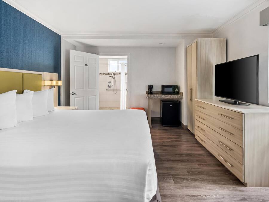 Habitación de hotel con una cama grande, televisión, minibar y baño visible a través de una puerta abierta.