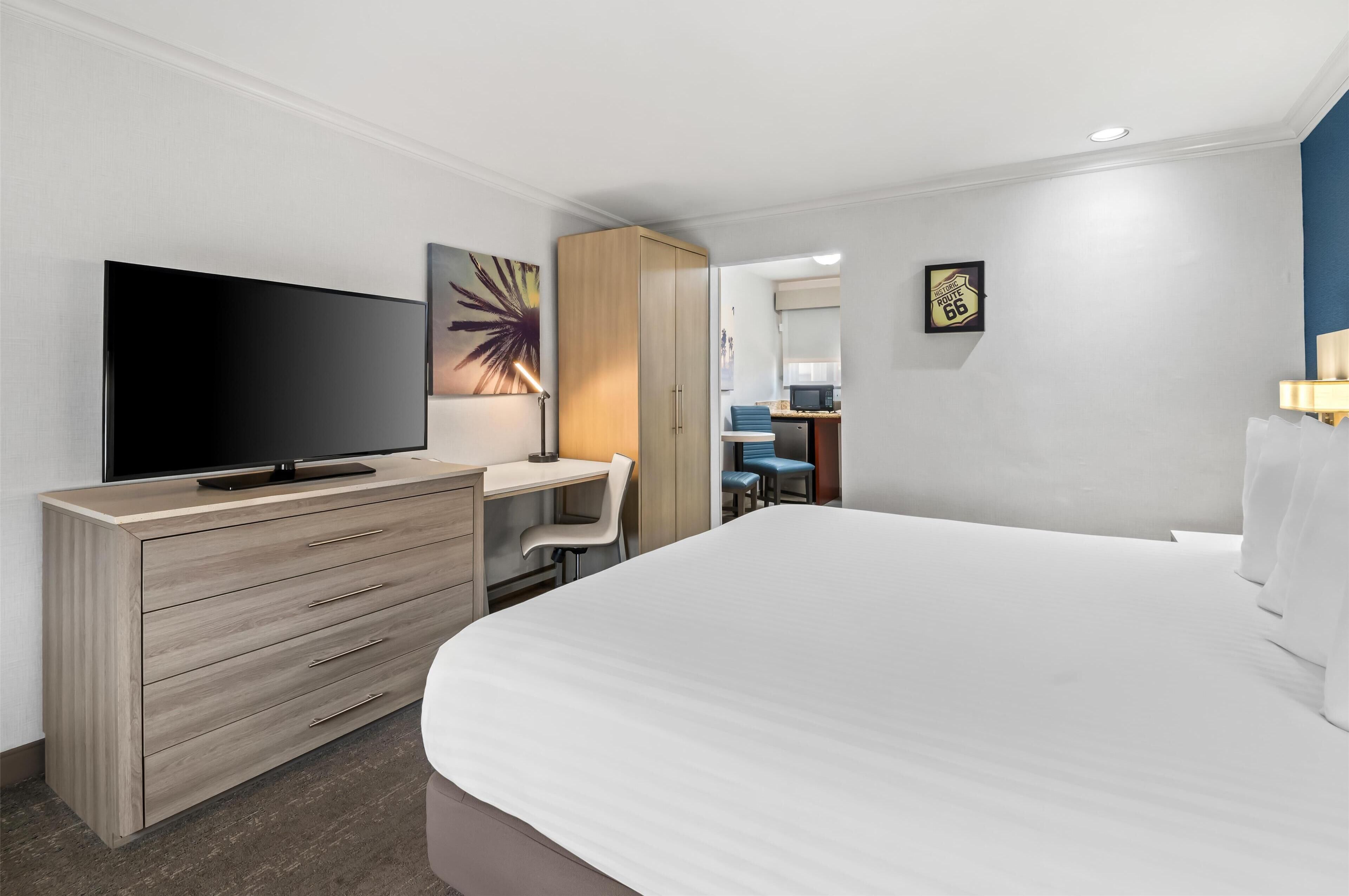A hotel room with a large bed, a TV on a wooden dresser, a desk with a chair, and a painting on the wall.