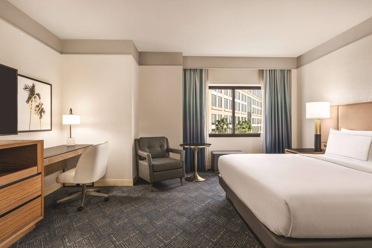 A hotel room with a bed, desk, chair, and a small table.