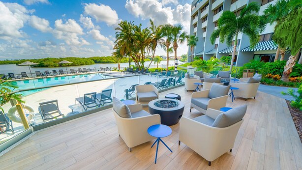 A rooftop pool area with lounge chairs, a fire pit, and a view of the water and palm trees. - DoubleTree by Hilton Tampa Rocky Point Waterfront (Tampa)