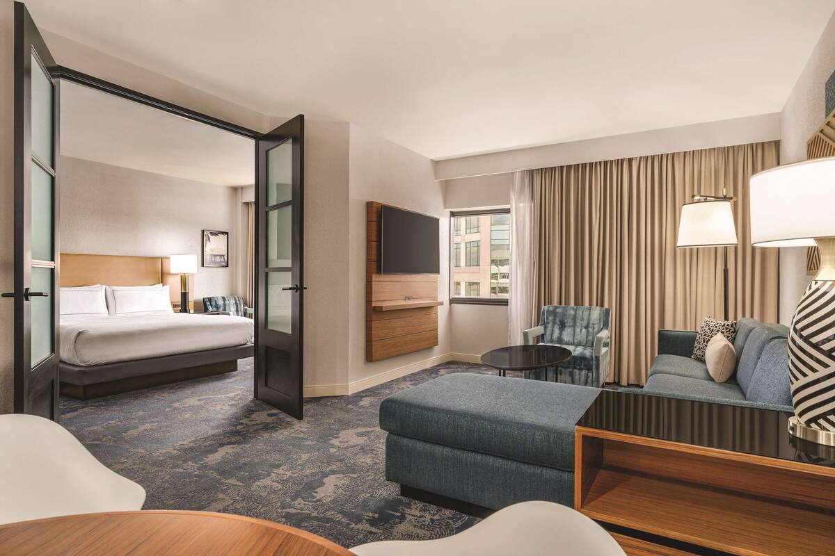 A hotel room with a bed, a sofa, a chair, a TV, and a window with curtains.