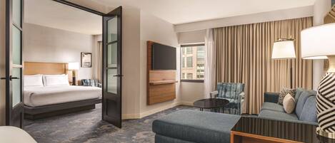 A hotel room with a bed, a sofa, a chair, a TV, and a window with curtains.