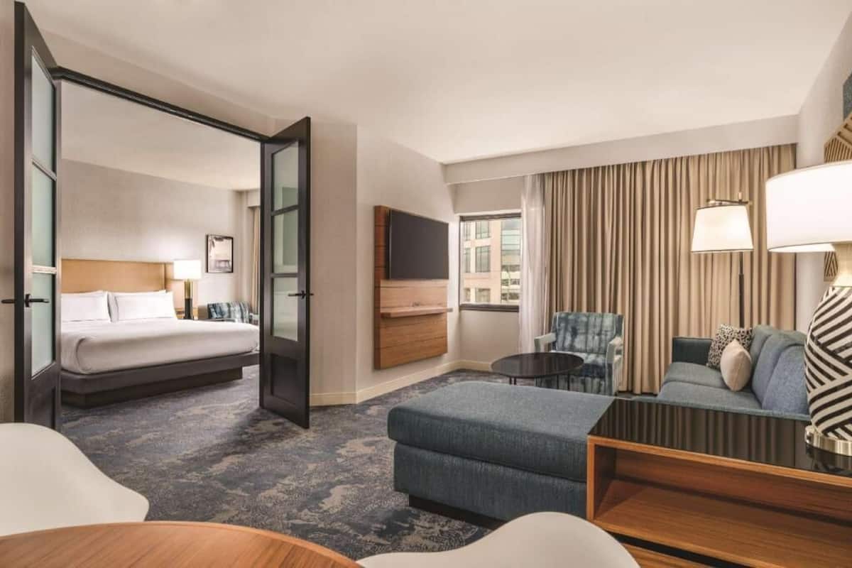 A hotel room with a bed, a sofa, a chair, a TV, and a window with curtains.