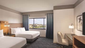 A hotel room with two beds, a desk, a chair, a window with a view, and a lamp.