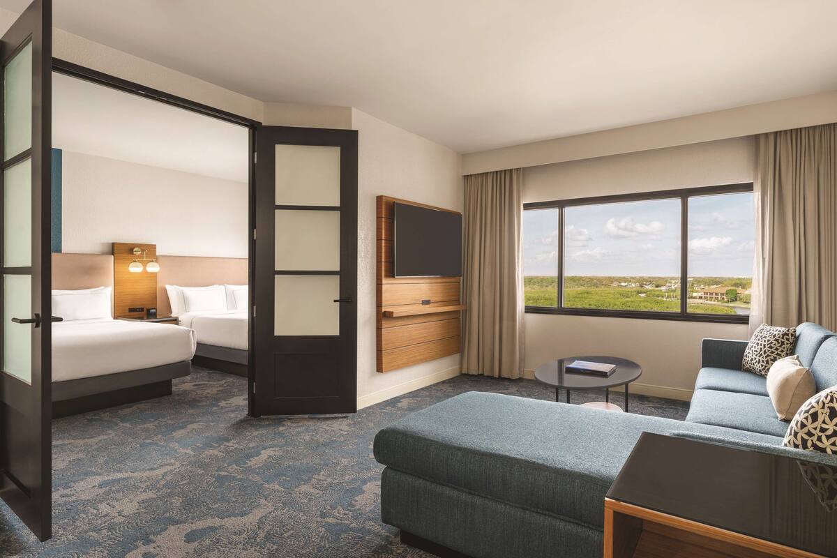 A hotel room with a bed, a sofa, a TV, a small table, and a window with a view of the landscape.