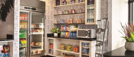 Una kitchenette equipada con refrigerador, microondas y estantes llenos de botanas y condimentos.