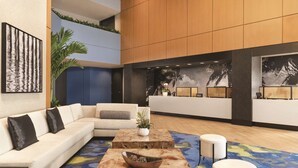 A modern lobby with a sectional sofa, a coffee table, and a reception desk. - DoubleTree by Hilton Tampa Rocky Point Waterfront (Tampa)
