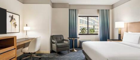 Habitación de hotel con cama, escritorio, silla y vistas a edificios a través de la ventana.