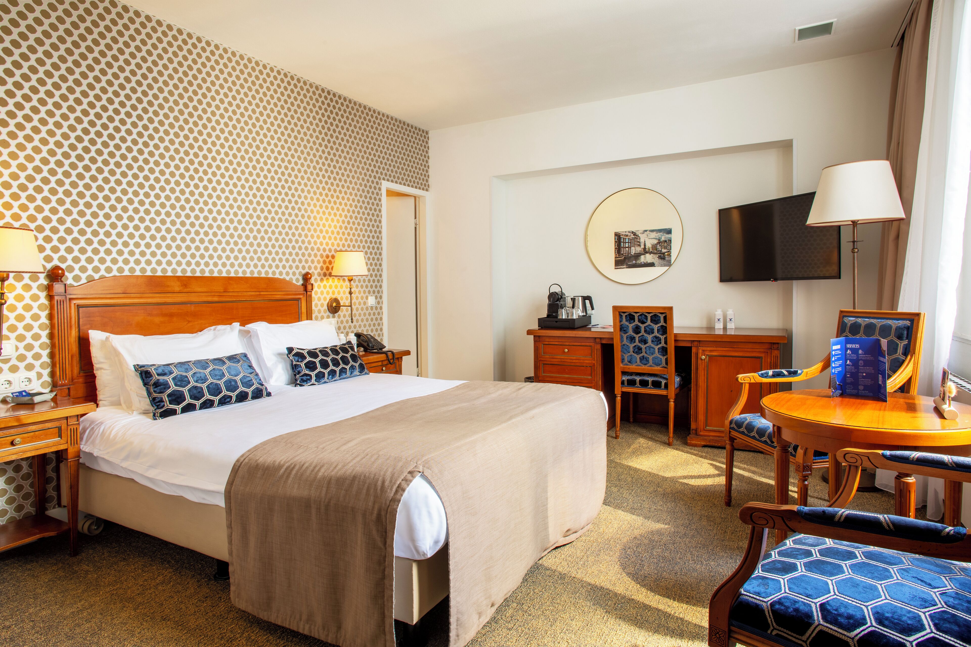 A hotel room with a large bed, a desk, a chair, a television, and a patterned wall.