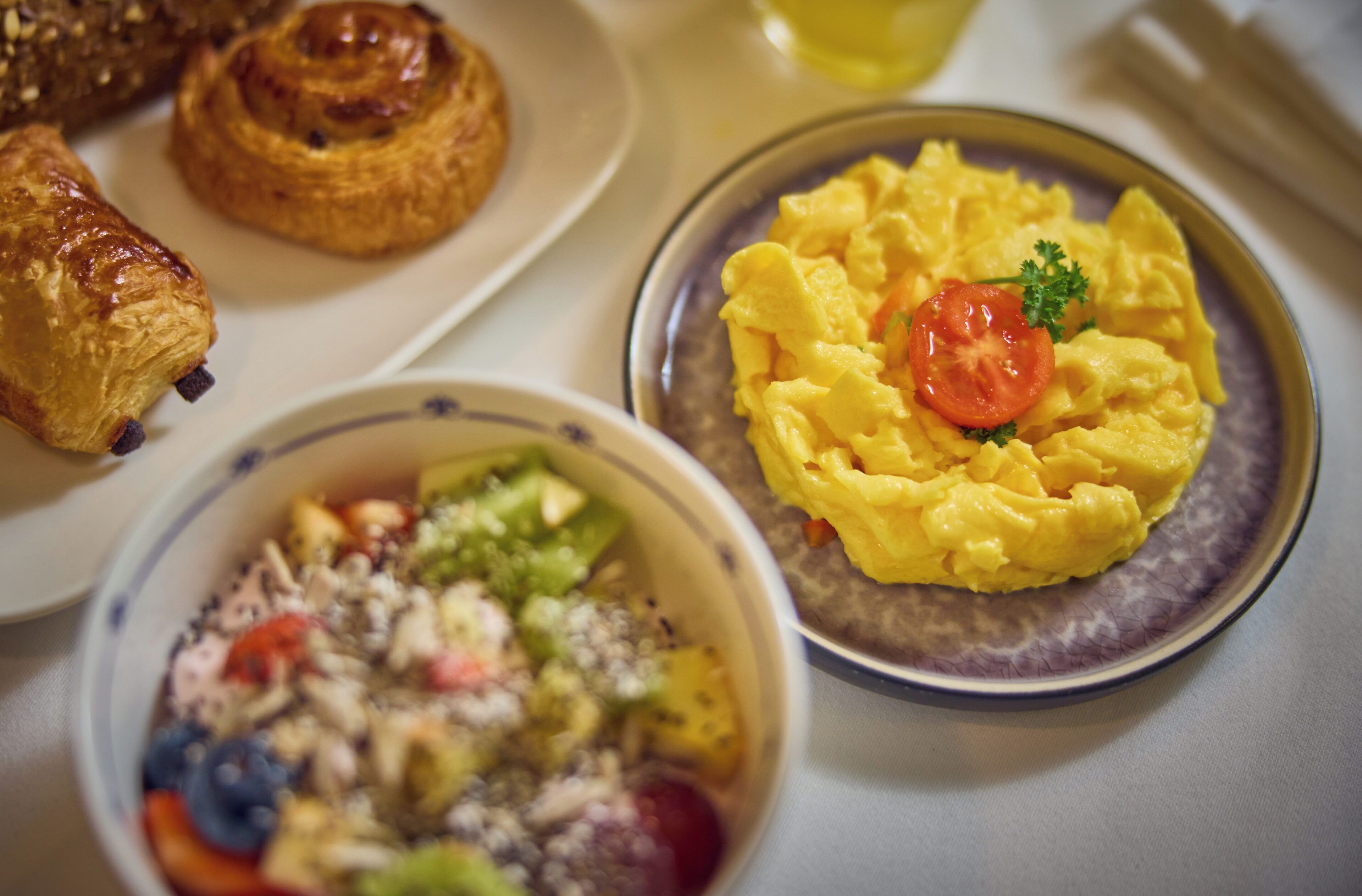 Une table dressée pour le petit-déjeuner avec des croissants, des œufs brouillés et une salade de fruits.