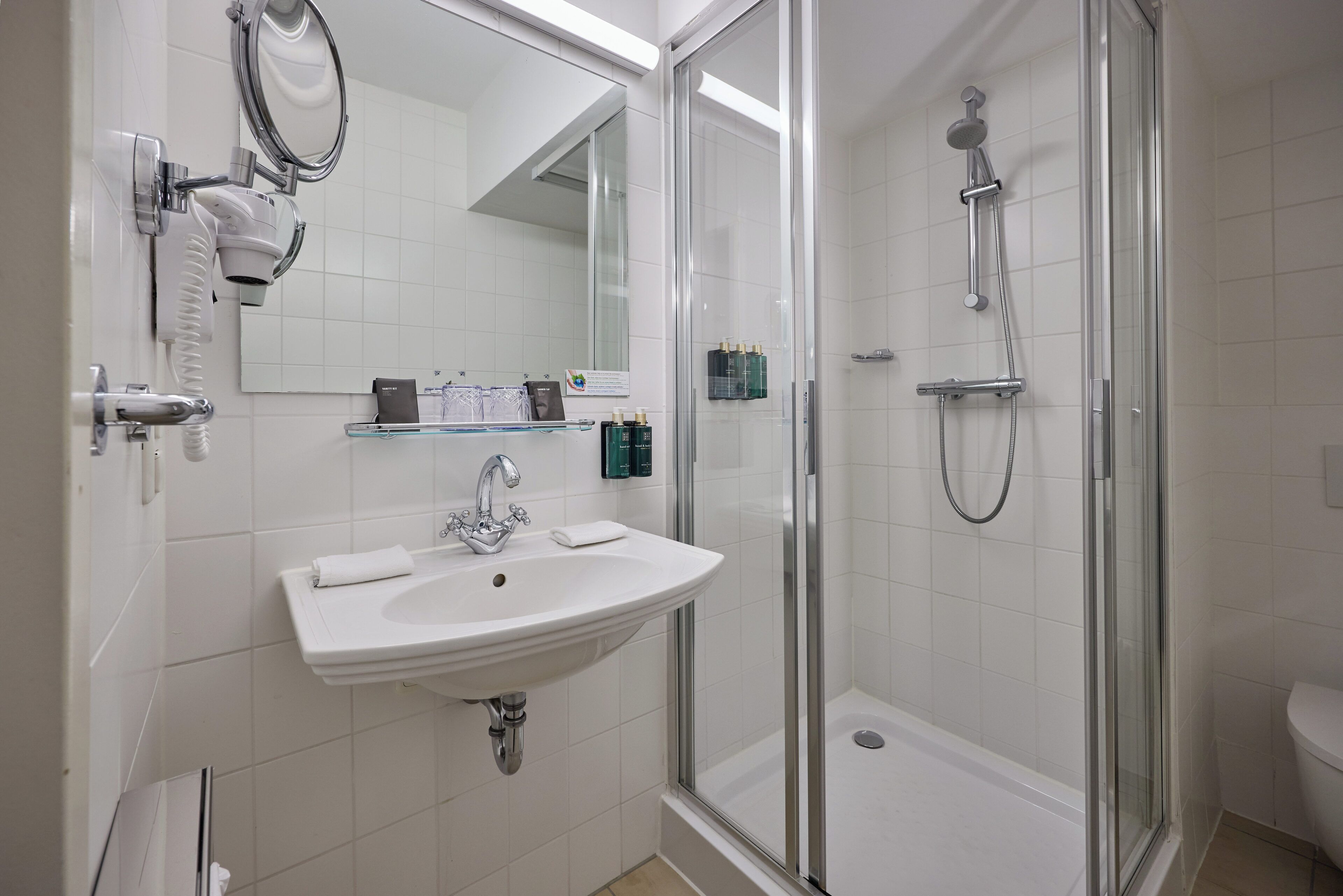 Un baño con un lavabo blanco, un espejo, cerramiento de ducha de vidrio y un inodoro.
