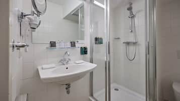 Un baño con un lavabo blanco, un espejo, cerramiento de ducha de vidrio y un inodoro.