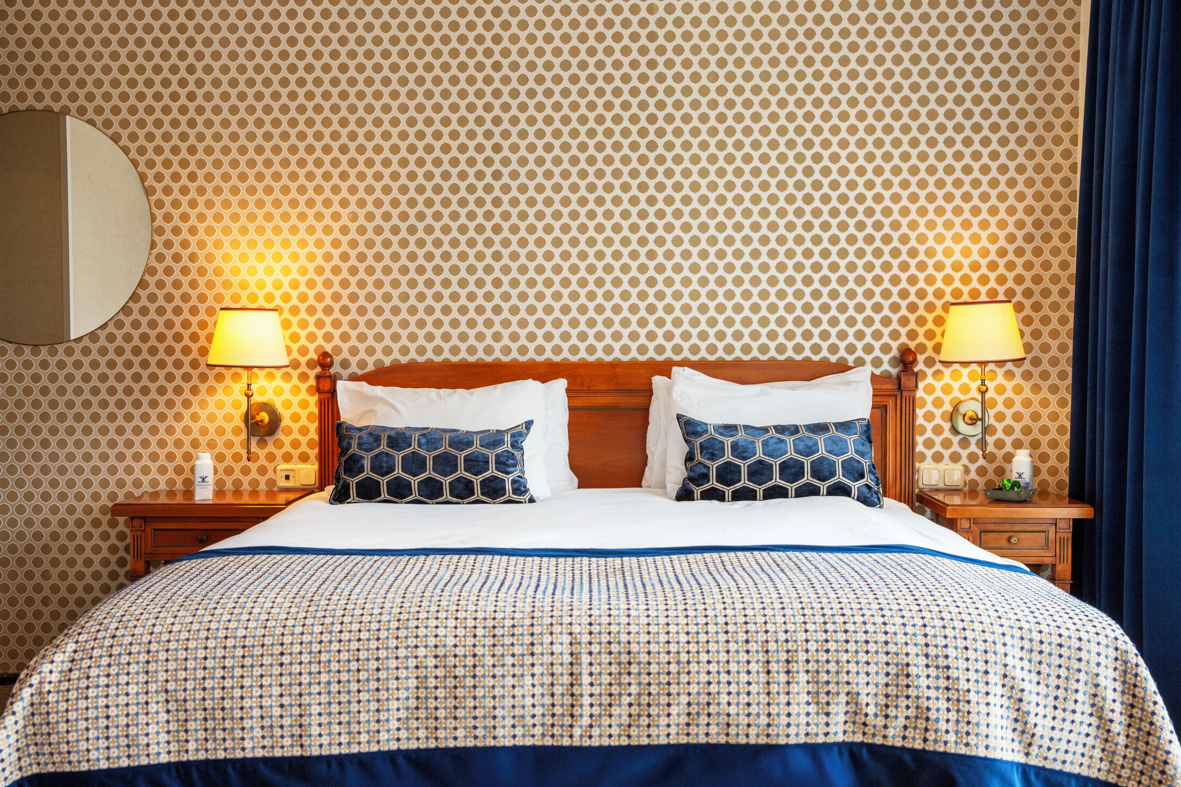A neatly made bed with a patterned bedspread, two bedside tables with lamps, and a wall with a geometric pattern.
