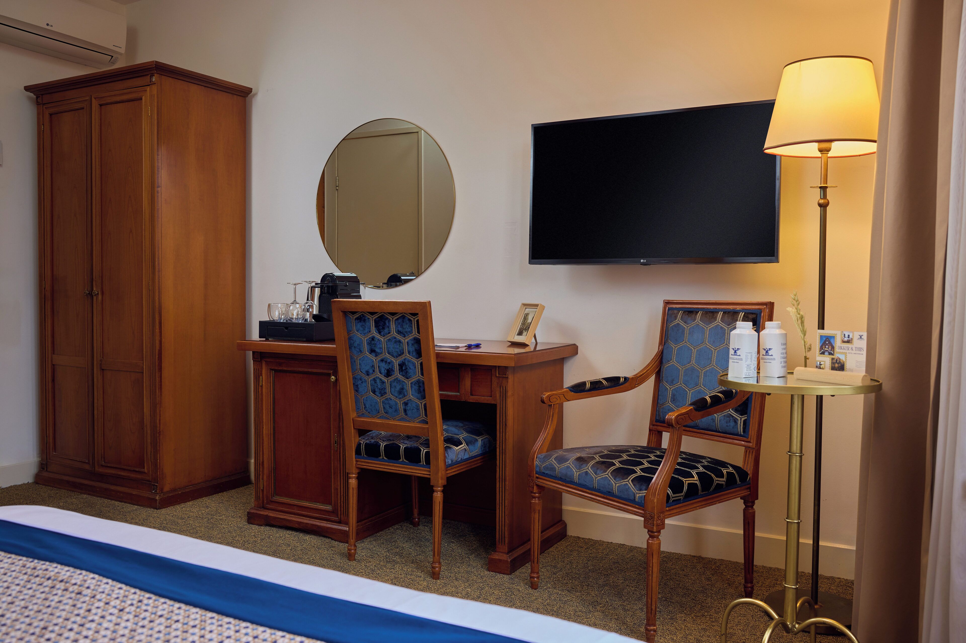 Habitación de hotel con una cama, un escritorio con silla, un armario, un televisor y una lámpara.