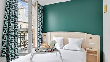 Una habitación de hotel con una cama, una mesita de noche con una bandeja de desayuno, una lámpara y vistas al balcón exterior.