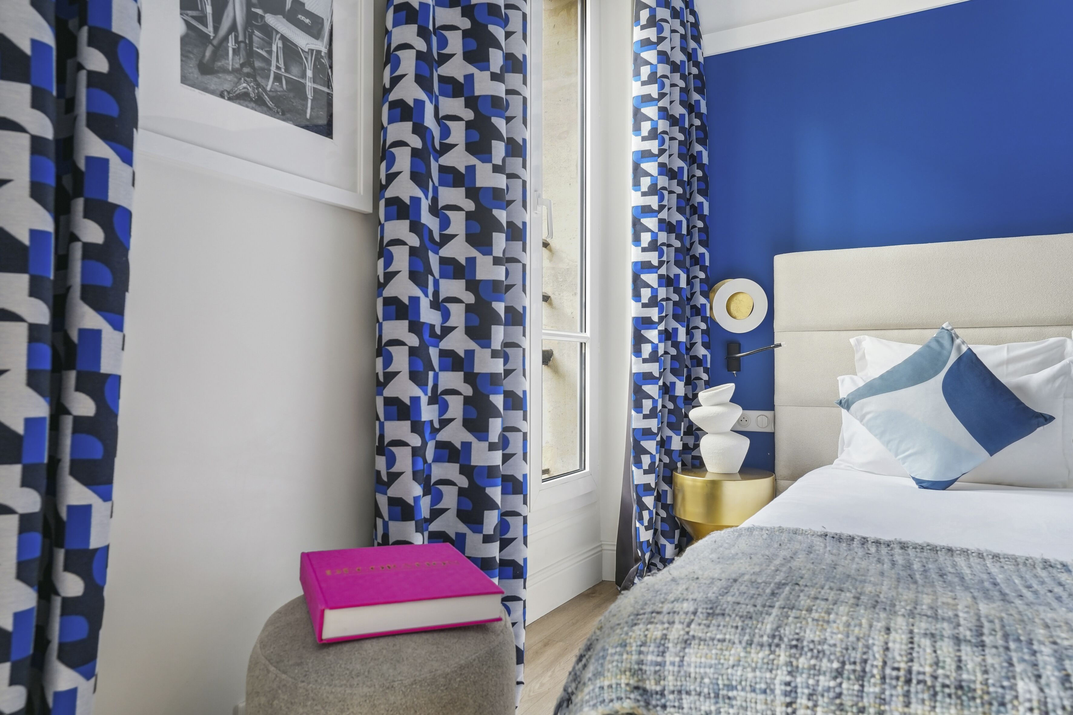 A bedroom with a bed, a bedside table, a lamp, and a window with curtains.