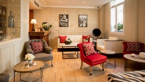A cozy living room with a stone wall, a sofa, a red armchair, and a coffee table. - Hôtel Elysées Opéra (Paris)