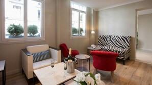 A modern living room with a sofa, red armchair, and a zebra-patterned chair. There is a table with a bottle of champagne and glasses. - Hôtel Elysées Opéra (Paris)