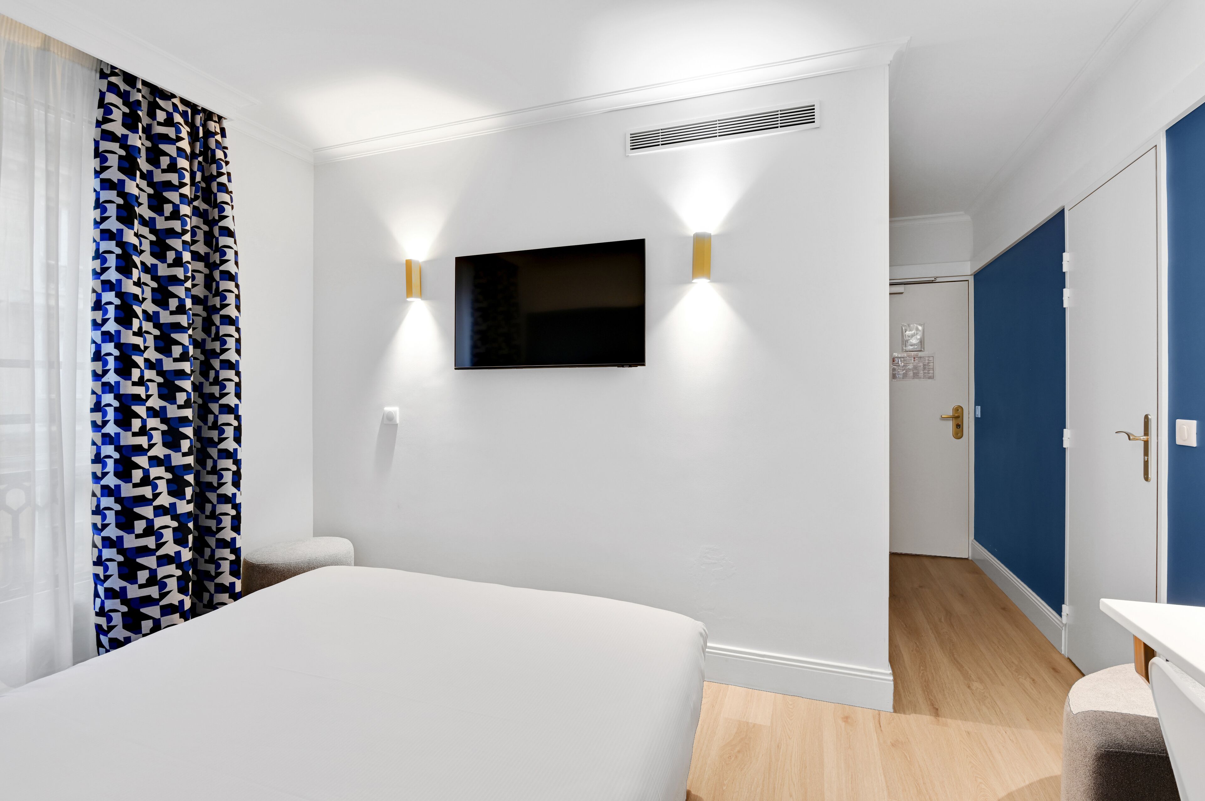 Une chambre d’hôtel équipée d’un lit, d’un téléviseur à  écran plat fixé au mur et d’une porte donnant accès à une salle de bain.