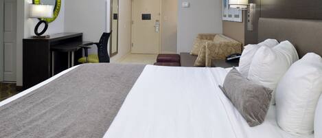 A hotel room with a large bed, a desk, a chair, and a small sofa.