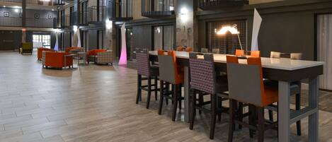 A spacious indoor area with multiple dining tables and chairs, a wooden floor, and a high ceiling with exposed beams and balconies.