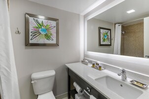 Un baño moderno con inodoro, lavamanos con espejo y dos cuadros abstractos enmarcados en la pared.
