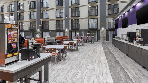 A spacious indoor dining area with multiple tables and chairs, a food service counter, and a modern architectural design with balconies.