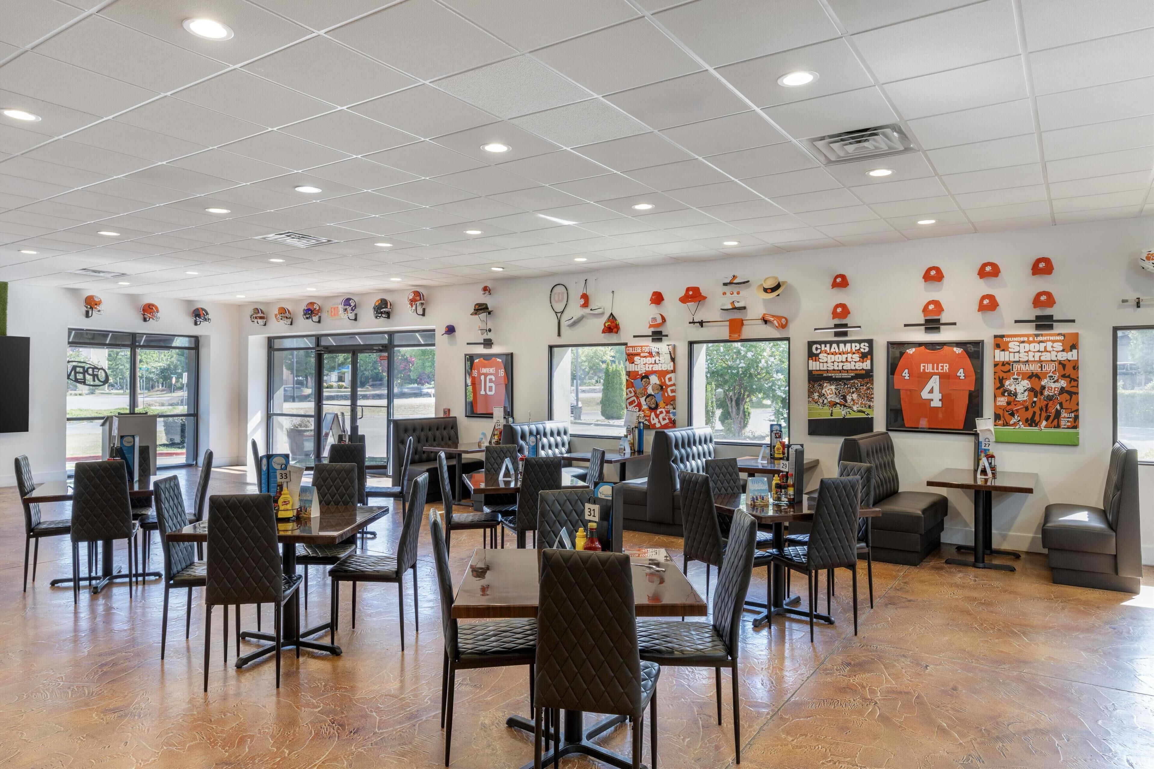 Un restaurant spacieux doté de plusieurs espaces de restauration, notamment des tables et des banquettes, et dont les murs sont ornés d’une variété de souvenirs et d’objets liés au sport.