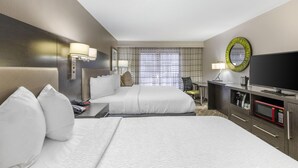 A hotel room with two beds, a television, a microwave, and a desk with a lamp.