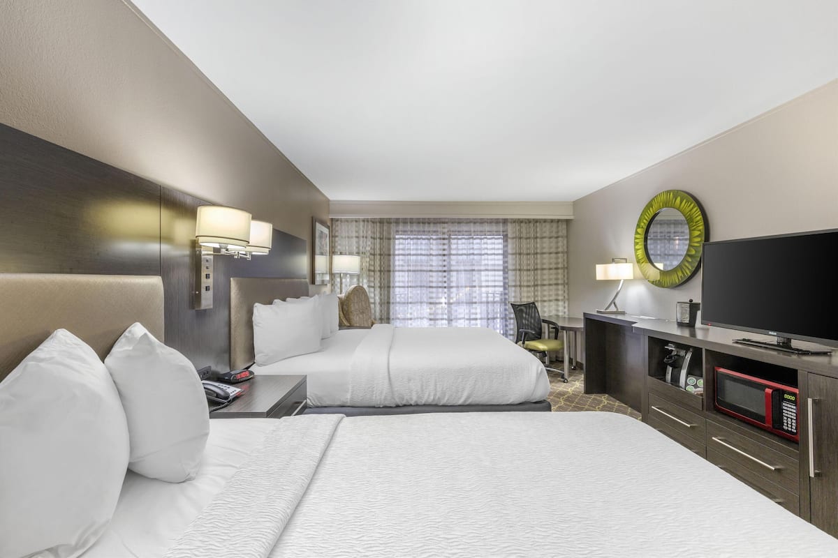 A hotel room with two beds, a television, a microwave, and a desk with a lamp.