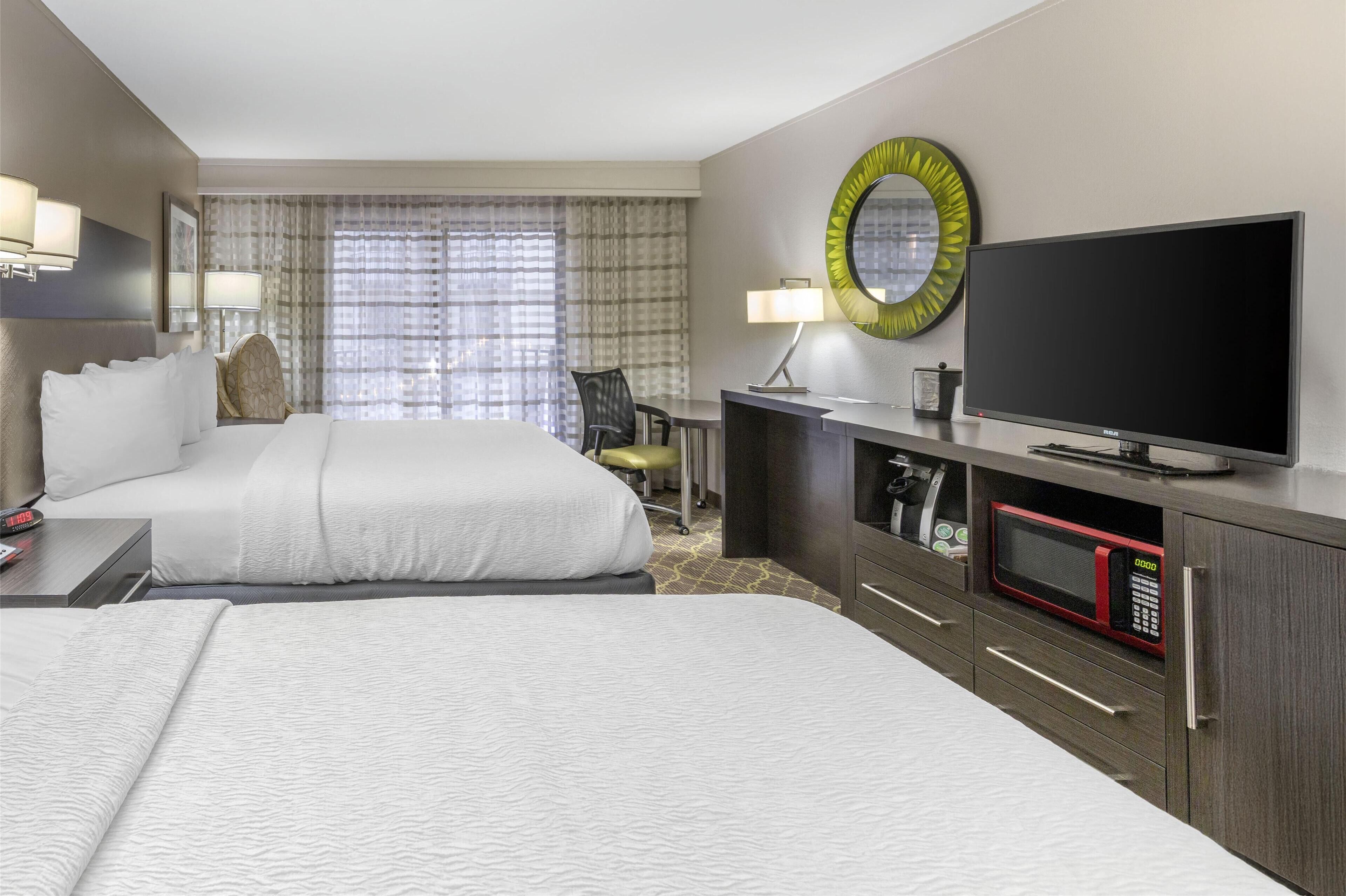 Habitación de hotel con dos camas, un escritorio, televisor, microondas y un espejo grande.