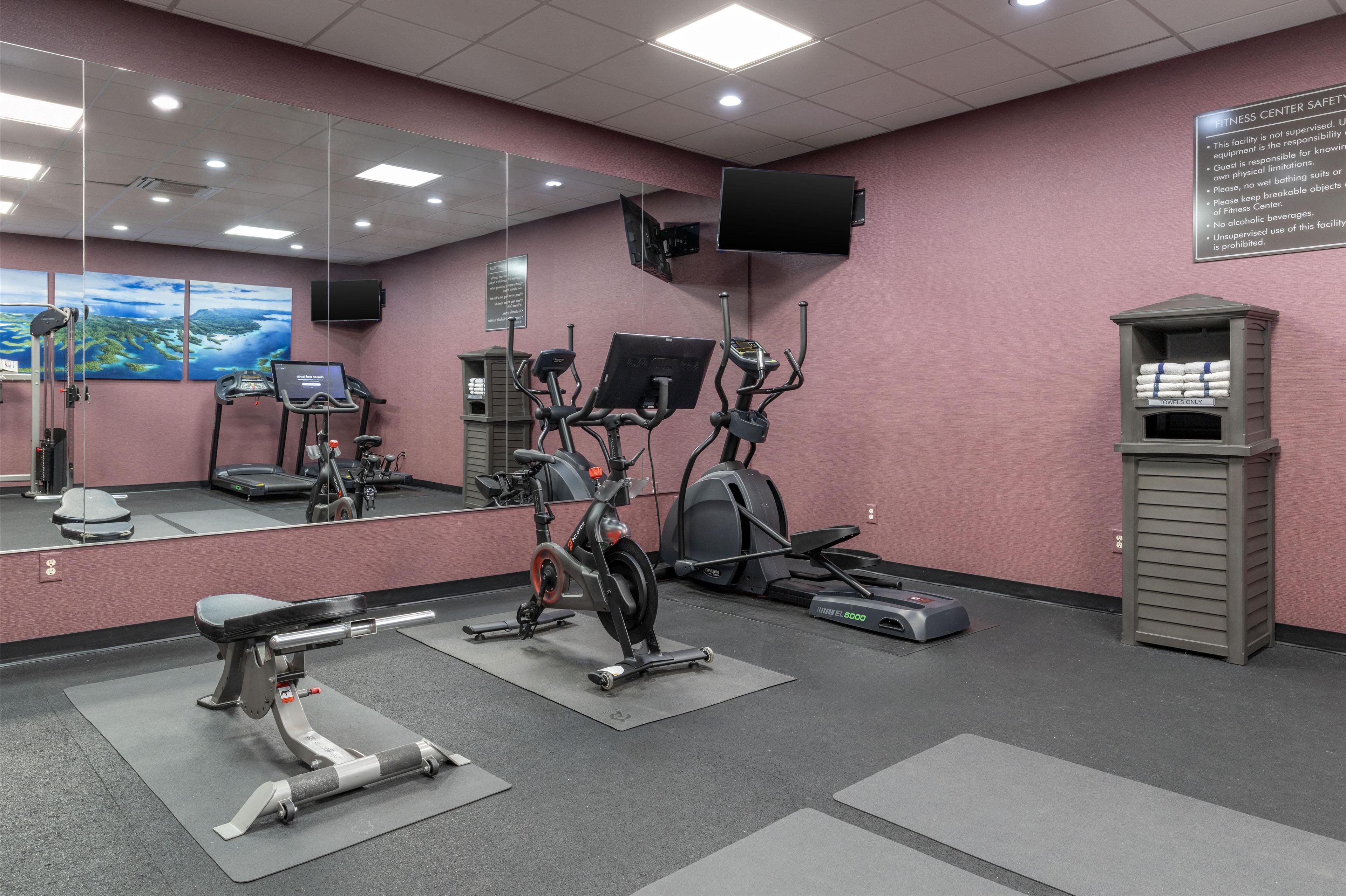 A fitness center with cardio machines, a weight bench, and a mirrored wall.
