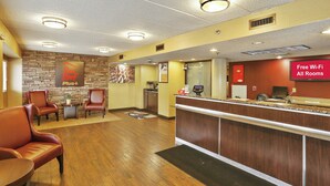 A hotel reception area with a stone wall, leather chairs, a reception desk, and a sign indicating free Wi-Fi.