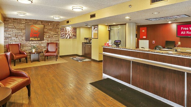 A hotel lobby with leather chairs, a reception desk, a Red Roof Plus sign, and a 'Free Wi-Fi All Rooms' sign.