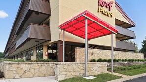 A Red Roof Plus hotel with a stone facade, multiple balconies, and a covered entrance.