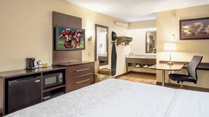 Une chambre d’hôtel comprenant un lit, un bureau, une télévision, un miroir et une salle de bain.