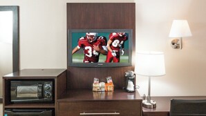Une chambre d’hôtel équipée d’une télévision diffusant un événement sportif, d’un bureau avec une lampe, d’une chaise et d’un mini-bar.