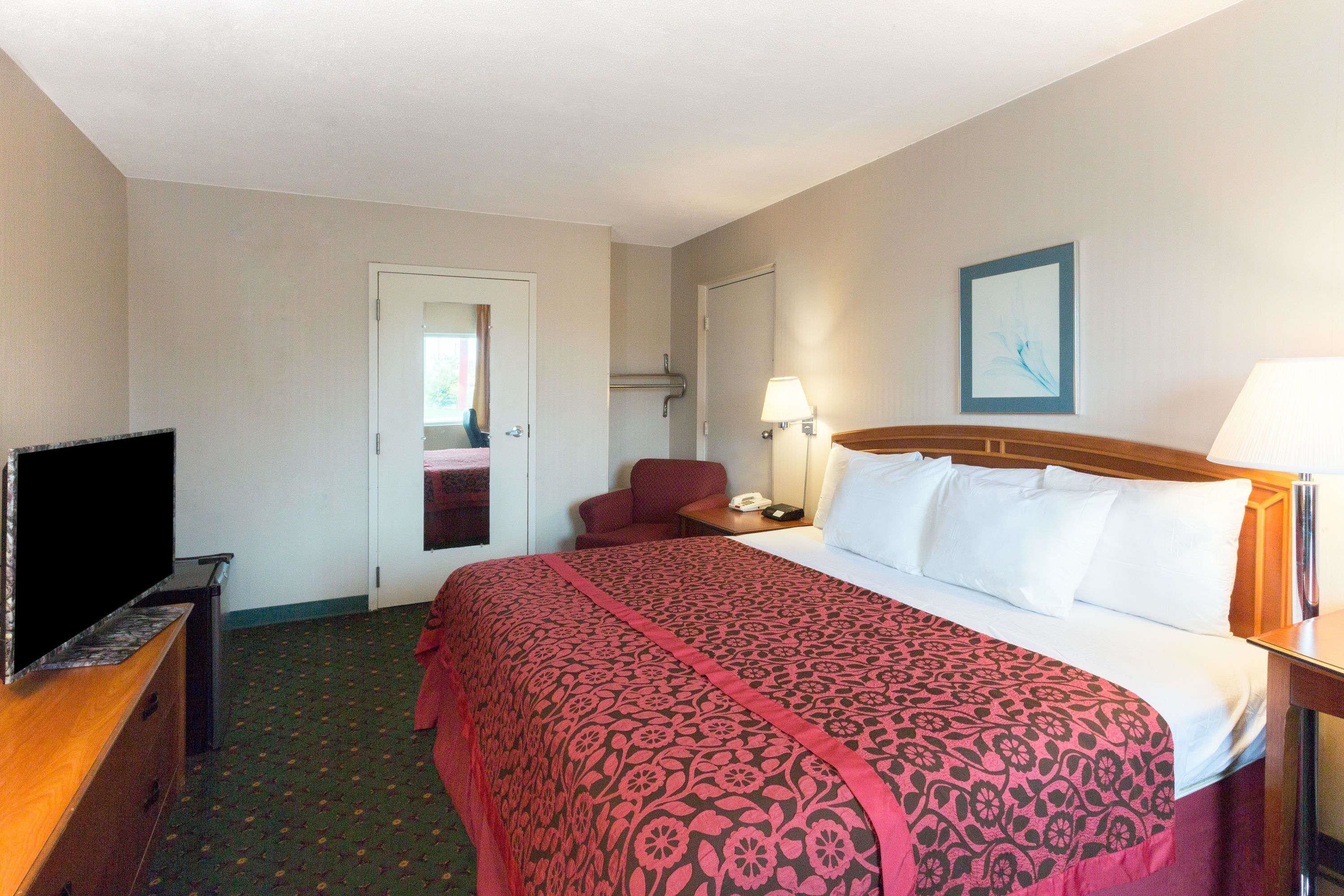 A hotel room with a bed, a TV, a desk, a chair, and a door leading to another room.