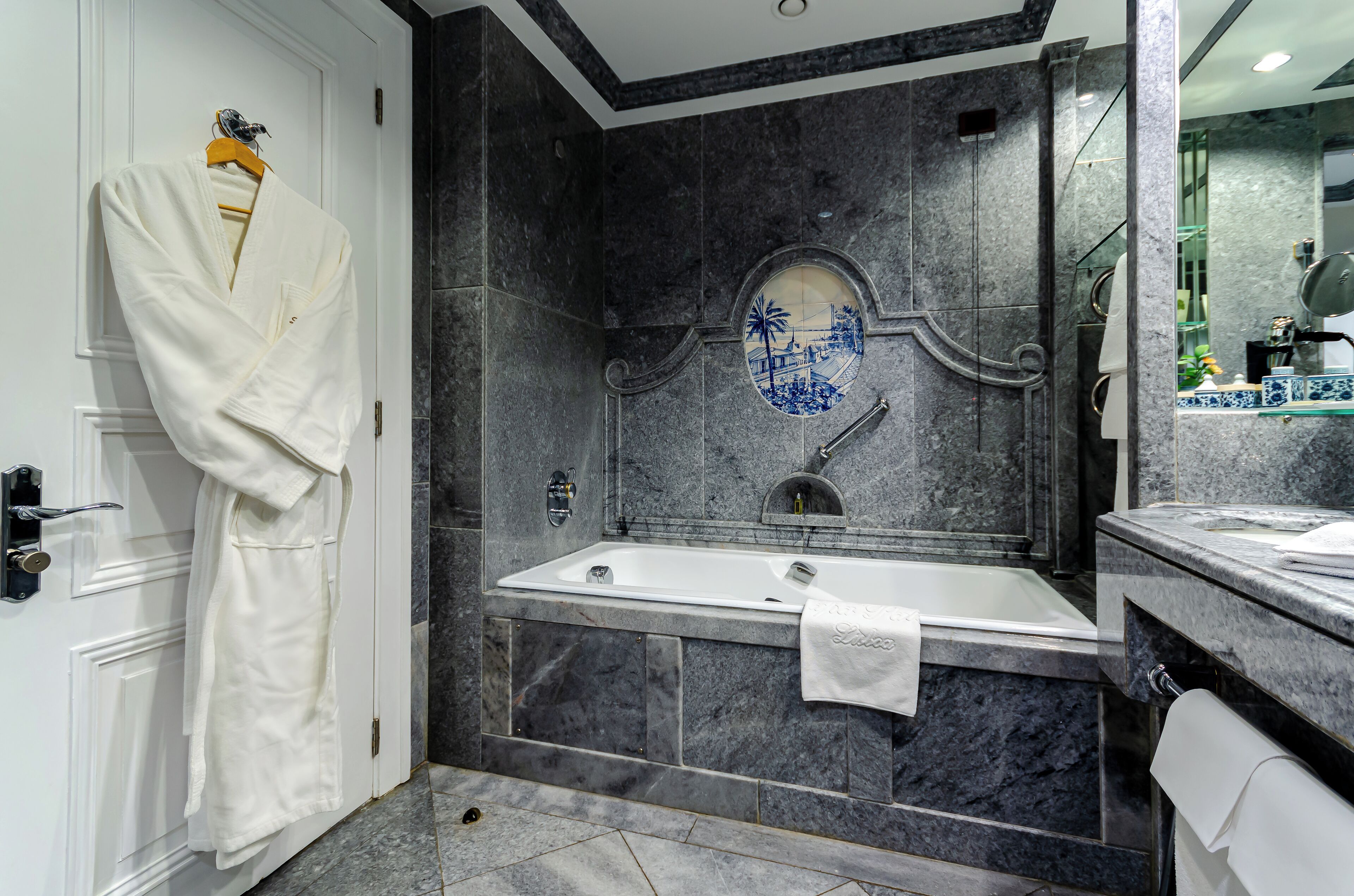 A bathroom with a bathtub, a mirror, and a robe hanging on the door.