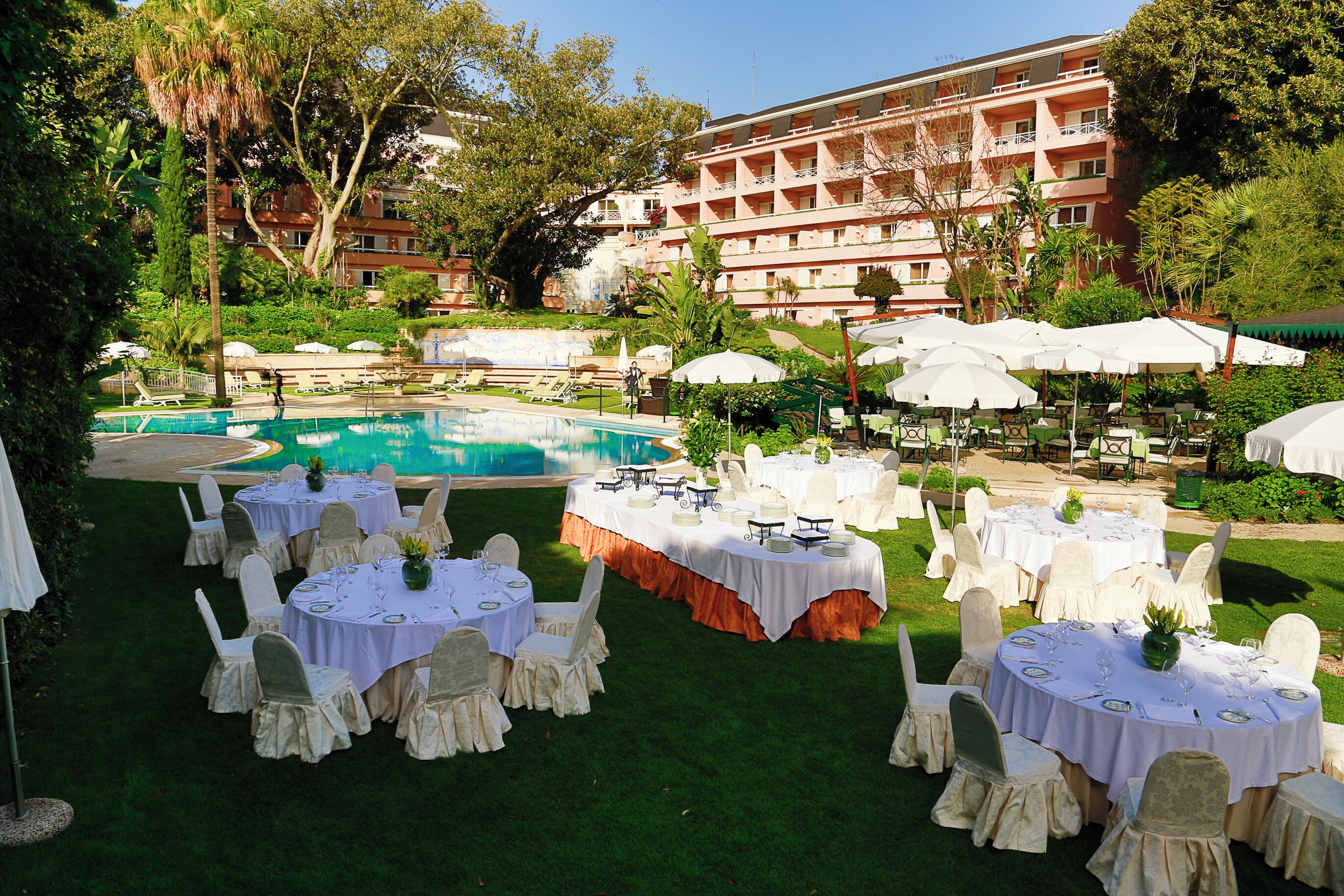 A poolside dining area with round tables, white chairs, and umbrellas.