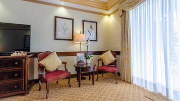 Une chambre d’hôtel avec un bureau en bois, deux fauteuils rouges à revêtement en tissu, une petite table avec une lampe et, au mur, des reproductions encadrées de gravures botaniques.