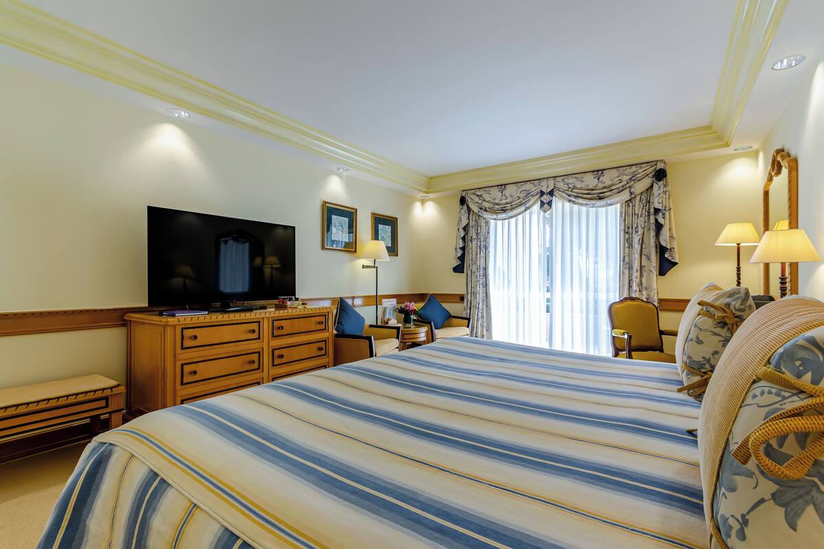 A hotel room with a large bed, a television, a desk, and a chair.