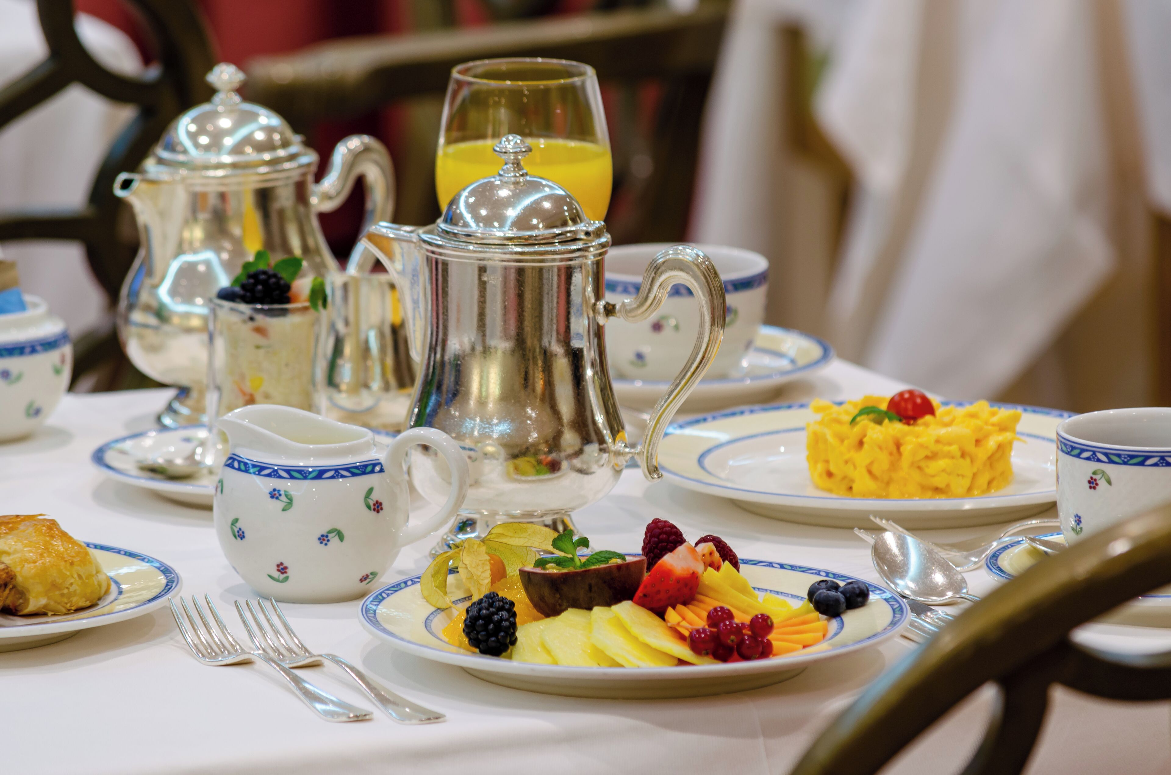 Una escena de desayuno con tetera, tazas, platos de fruta y huevos revueltos.