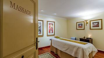 A massage room with a bed, framed pictures on the wall, and a door labeled "MASSAGE".