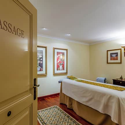 A massage room with a bed, framed pictures on the wall, and a door labeled "MASSAGE".