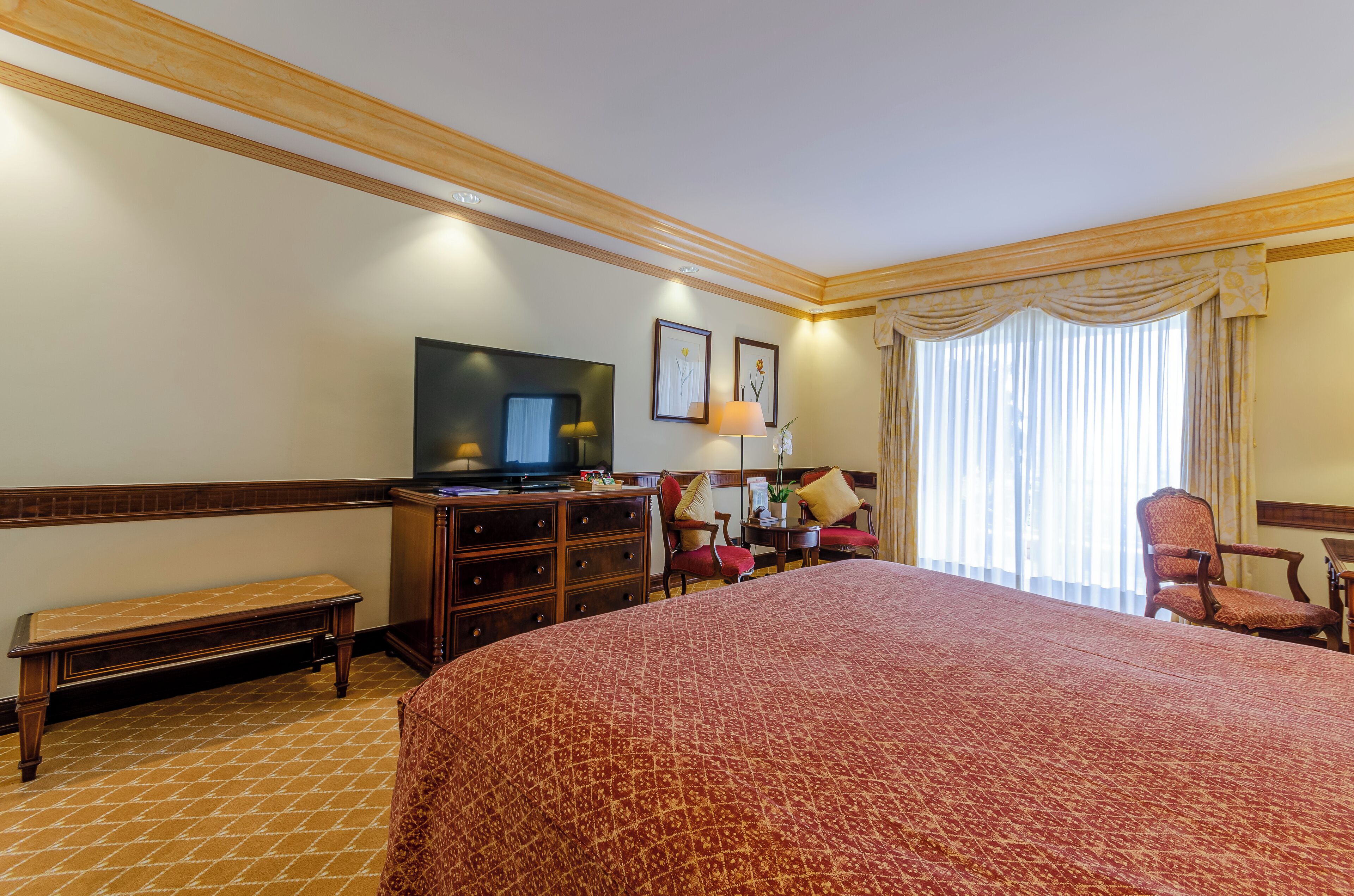 Una camera d'albergo con un letto grande, una televisione, una scrivania con una lampada e una sedia.