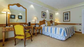 Habitación de hotel con cama, escritorio, silla, espejo y cuadros en la pared.